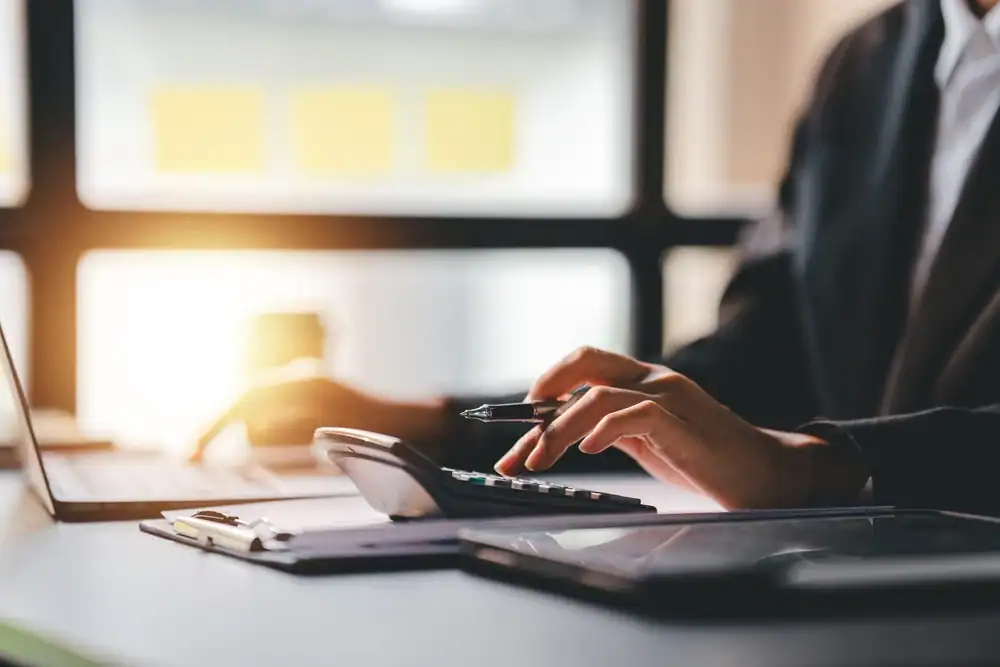 High-angle view of a person using a calculator and laptop at a desk, representing tax resolution services.