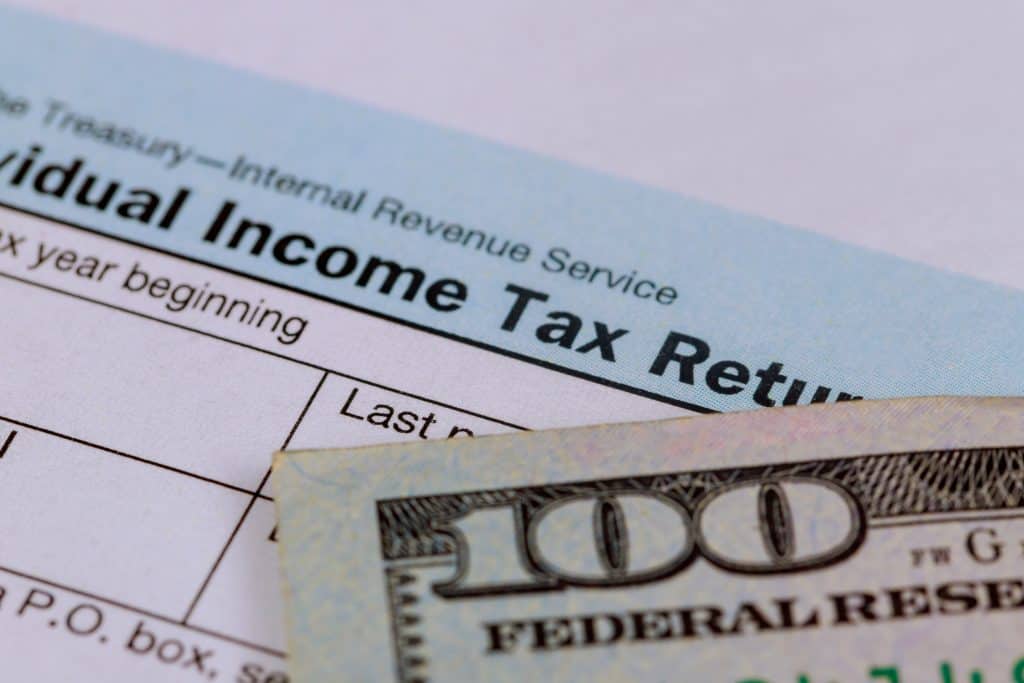A close-up of a U.S. Individual Income Tax Return form partially covered by a $100 bill, symbolizing taxation and finances.